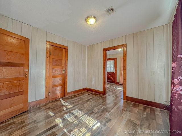 unfurnished room with wood-type flooring, a textured ceiling, and wooden walls