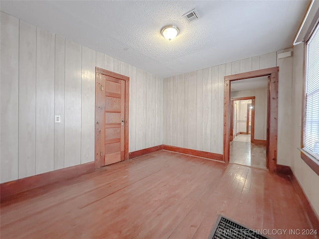 unfurnished room with wood walls, light hardwood / wood-style floors, and a textured ceiling