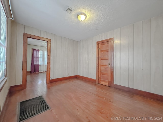 unfurnished room with wood-type flooring, a textured ceiling, and wooden walls