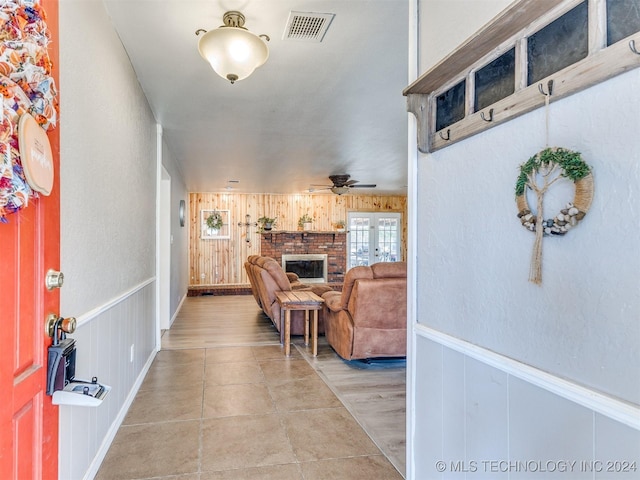 entrance foyer featuring light wood-type flooring, a brick fireplace, ceiling fan, and wood walls