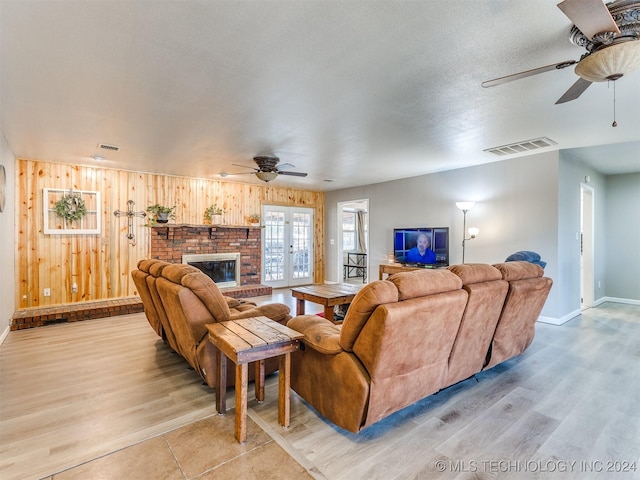 living room featuring ceiling fan, a brick fireplace, light hardwood / wood-style flooring, wood walls, and a textured ceiling