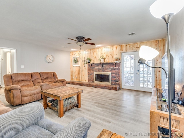 living room with french doors, light wood-type flooring, ceiling fan, a fireplace, and wood walls