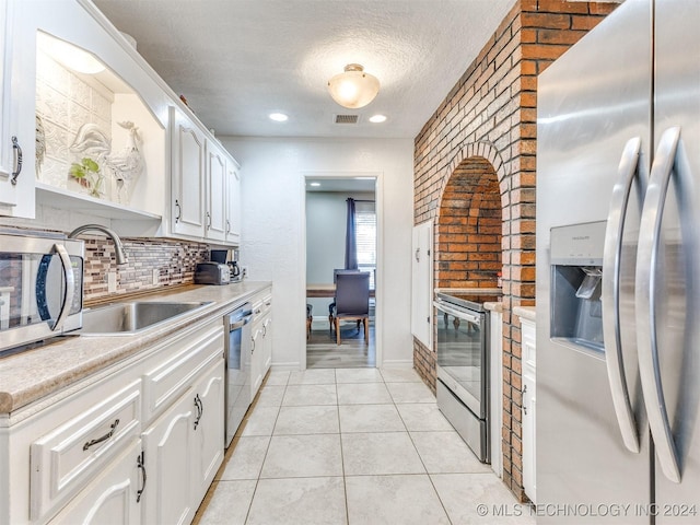 kitchen with white cabinetry, sink, brick wall, and appliances with stainless steel finishes