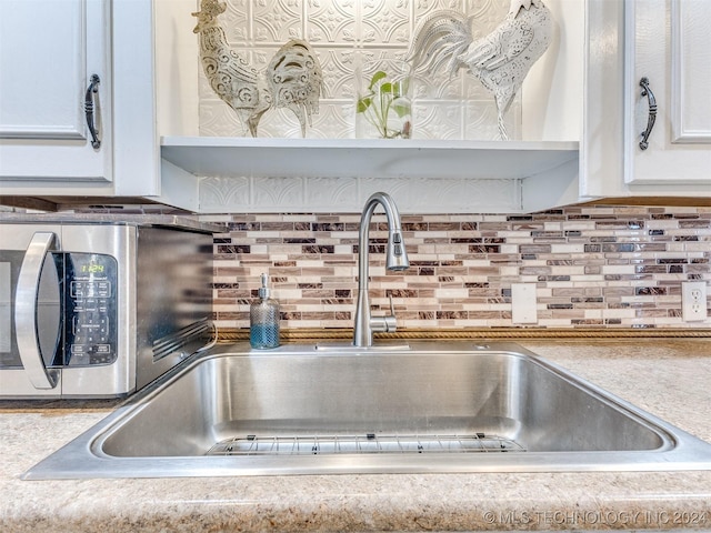 room details featuring white cabinetry, sink, and tasteful backsplash