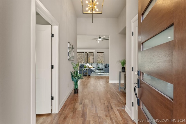 foyer entrance with light hardwood / wood-style flooring and ceiling fan with notable chandelier