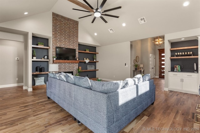 living room with wood-type flooring, ceiling fan with notable chandelier, high vaulted ceiling, and a brick fireplace