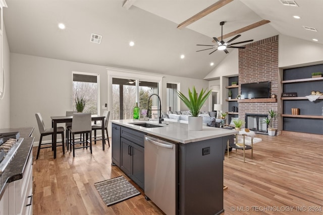 kitchen featuring sink, stainless steel appliances, light hardwood / wood-style floors, a fireplace, and a center island with sink