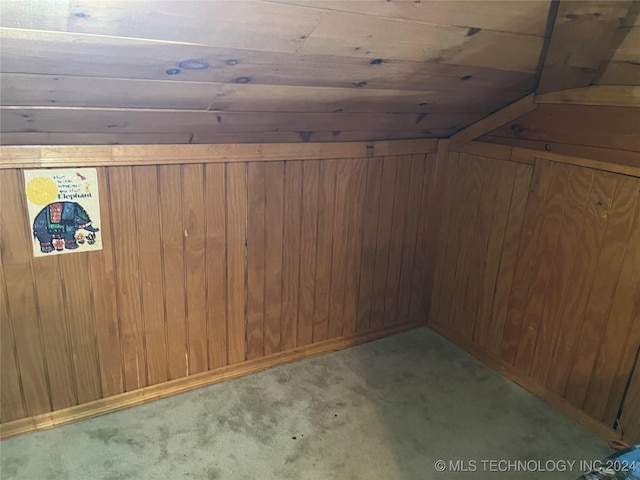 additional living space with wood walls, light colored carpet, and vaulted ceiling