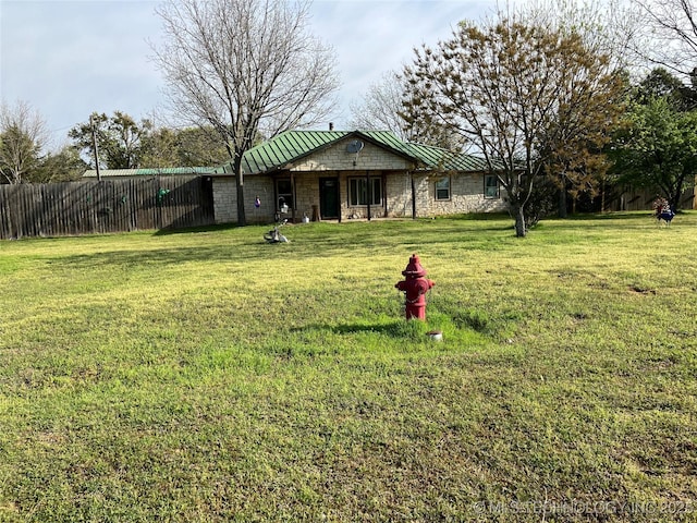 single story home featuring stone siding, a front lawn, a standing seam roof, metal roof, and fence
