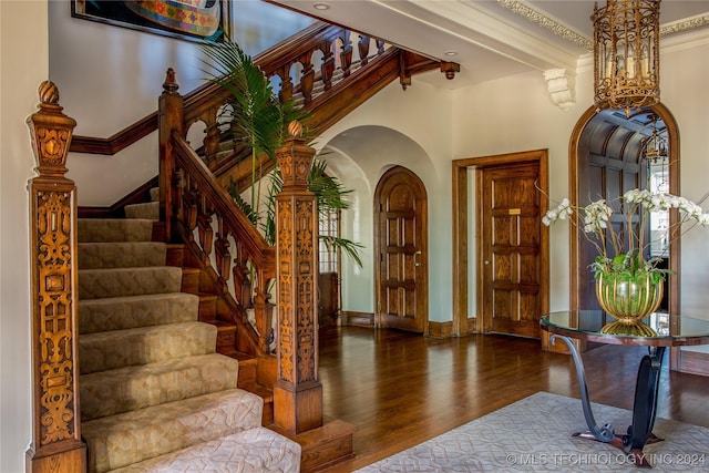 entrance foyer with ornamental molding, a towering ceiling, and dark wood-type flooring