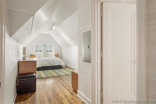 bedroom featuring lofted ceiling, wood-type flooring, and electric panel