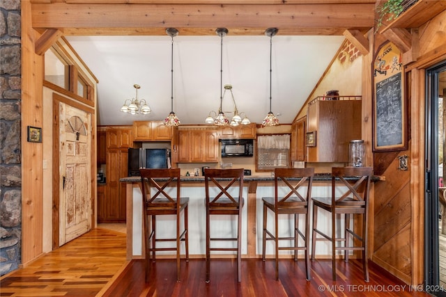 kitchen featuring dark wood-type flooring, an inviting chandelier, a kitchen breakfast bar, pendant lighting, and black appliances