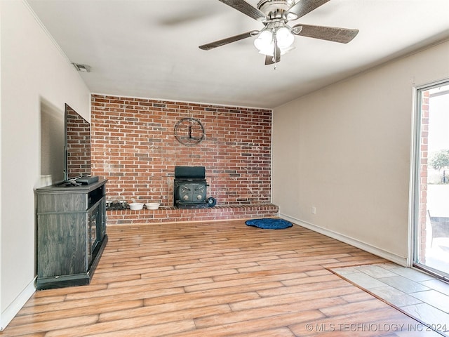 unfurnished living room with light hardwood / wood-style floors, ceiling fan, a healthy amount of sunlight, and a wood stove