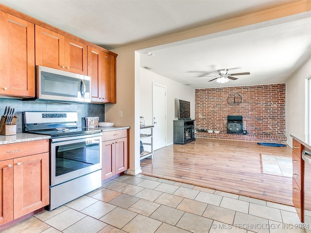 kitchen with a wood stove, light hardwood / wood-style flooring, ceiling fan, decorative backsplash, and stainless steel appliances