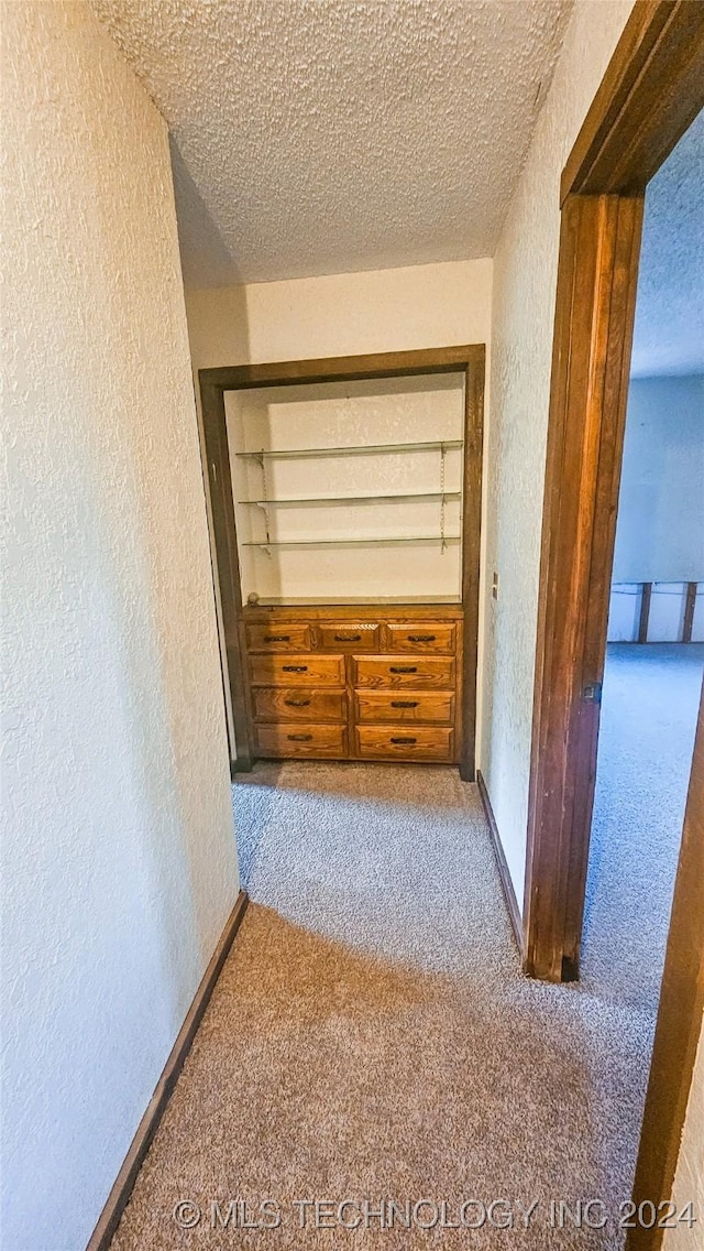 hallway featuring built in features, carpet floors, and a textured ceiling