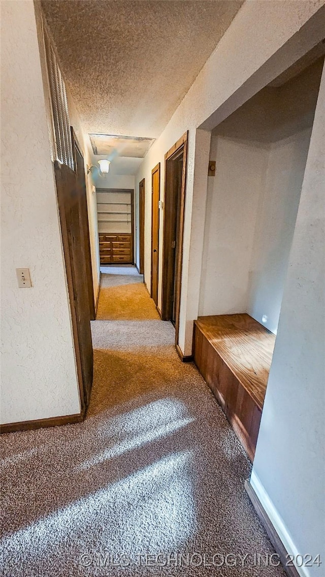 hall with light colored carpet and a textured ceiling