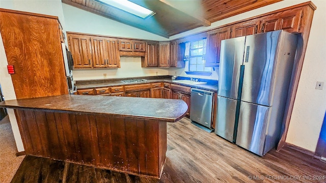 kitchen with lofted ceiling, stainless steel appliances, kitchen peninsula, and wood-type flooring