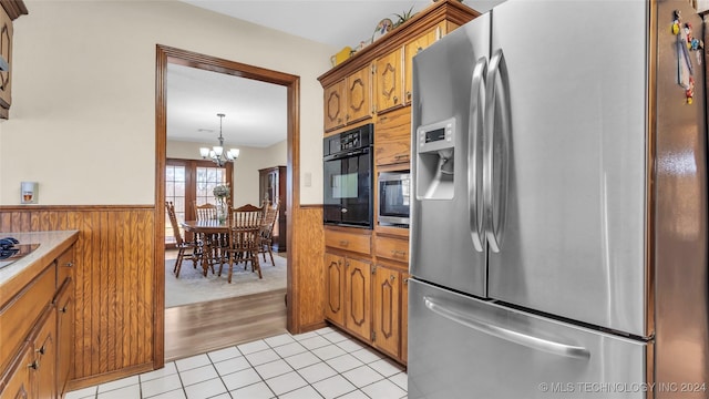 kitchen with hanging light fixtures, wooden walls, light tile patterned floors, appliances with stainless steel finishes, and a chandelier