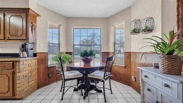 dining area featuring light tile patterned floors, a textured ceiling, and wooden walls