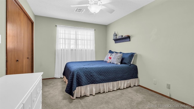 bedroom featuring ceiling fan, a closet, light carpet, and a textured ceiling