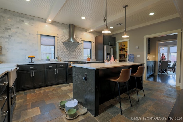 kitchen featuring beam ceiling, hanging light fixtures, wall chimney range hood, high quality fridge, and a kitchen island