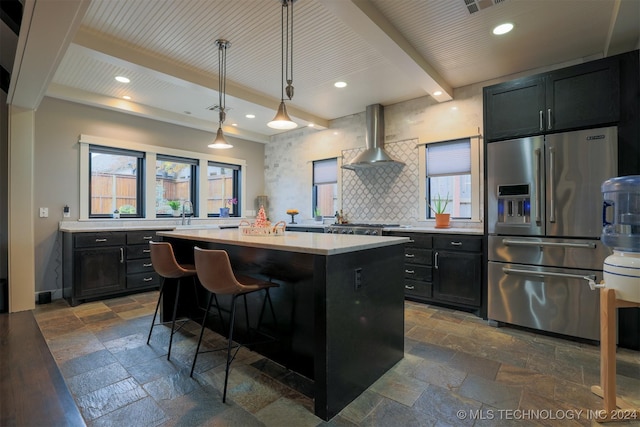 kitchen with a wealth of natural light, high quality fridge, wall chimney exhaust hood, decorative light fixtures, and a center island