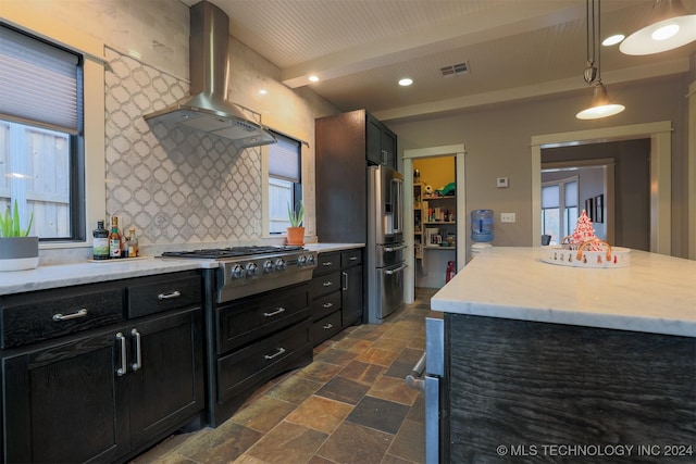 kitchen featuring beam ceiling, a center island, stainless steel appliances, wall chimney range hood, and decorative light fixtures