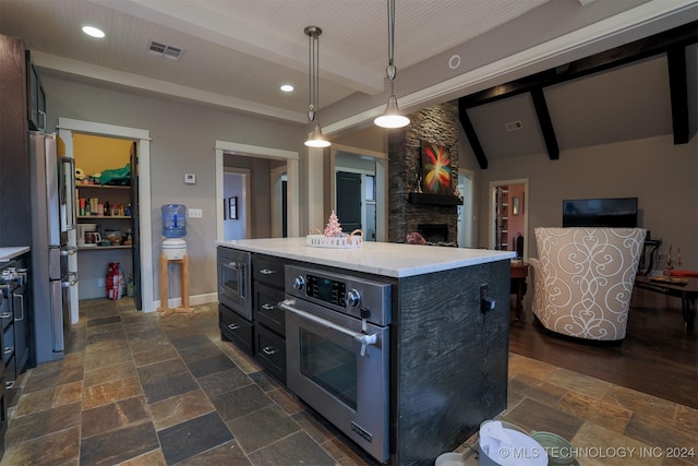 kitchen featuring appliances with stainless steel finishes, pendant lighting, lofted ceiling with beams, a kitchen island, and a stone fireplace