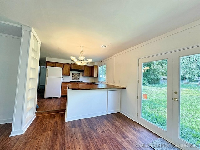 kitchen with hanging light fixtures, dark hardwood / wood-style floors, a notable chandelier, white refrigerator, and kitchen peninsula