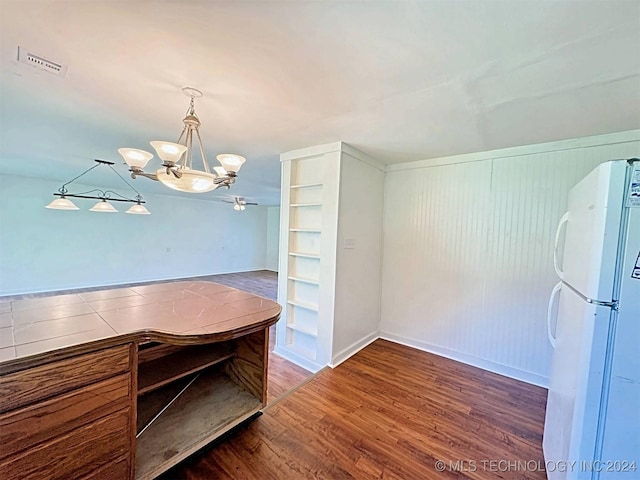 dining space with wood walls, ceiling fan with notable chandelier, and dark hardwood / wood-style floors