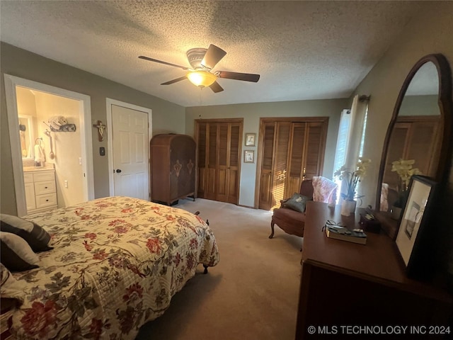 carpeted bedroom with a textured ceiling, two closets, ceiling fan, and ensuite bathroom