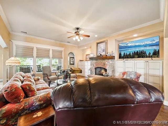 living room featuring wood-type flooring, a stone fireplace, ceiling fan, and ornamental molding