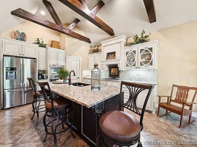 kitchen with a kitchen bar, stainless steel appliances, sink, white cabinetry, and an island with sink