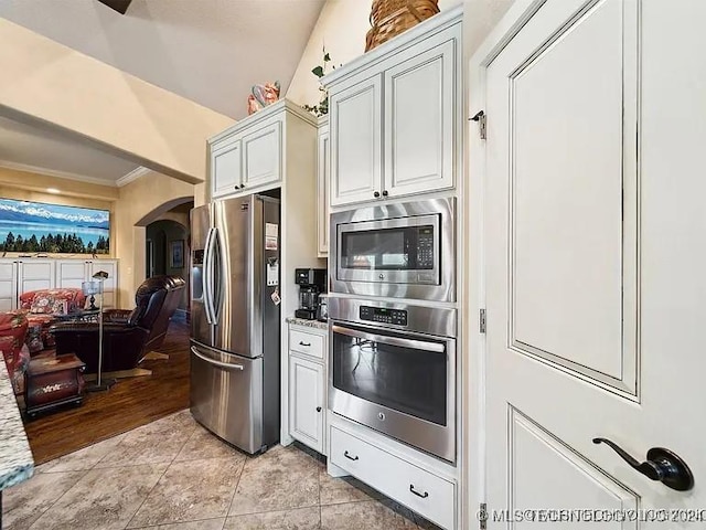 kitchen featuring white cabinetry, stainless steel appliances, light hardwood / wood-style floors, lofted ceiling, and ornamental molding