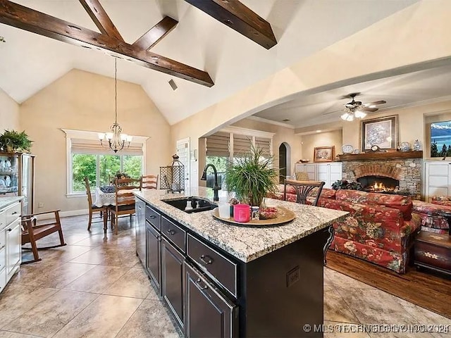 kitchen with light stone counters, a kitchen island with sink, sink, pendant lighting, and a fireplace