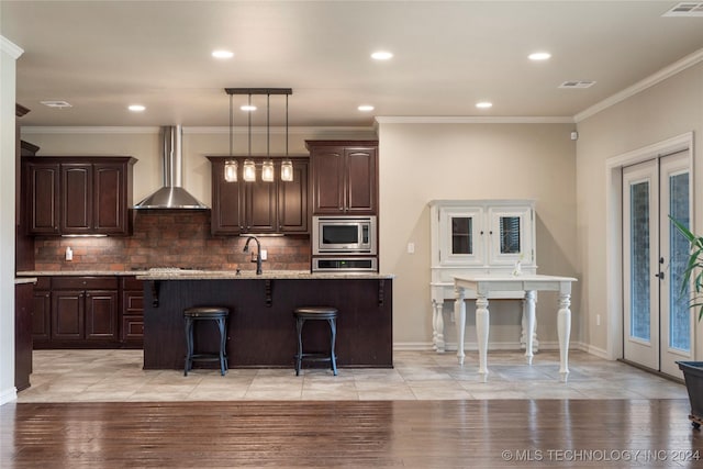 kitchen featuring a center island with sink, appliances with stainless steel finishes, wall chimney range hood, and light wood-type flooring