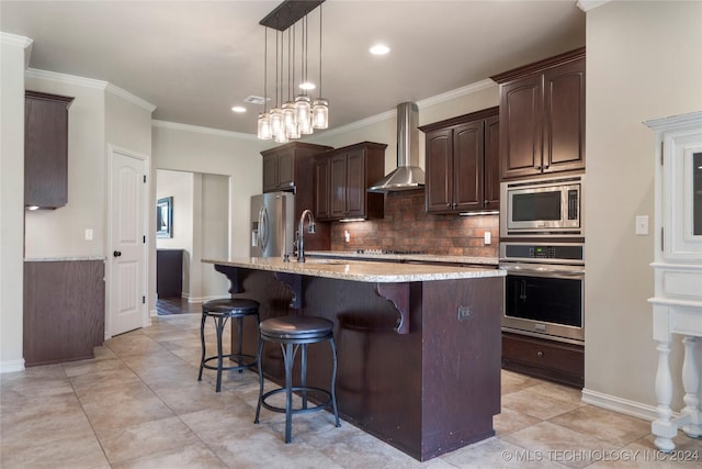 kitchen featuring sink, wall chimney range hood, an island with sink, decorative light fixtures, and appliances with stainless steel finishes