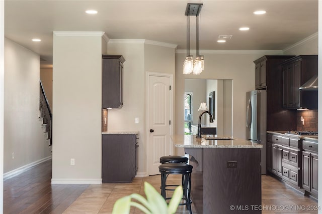 kitchen with sink, stainless steel appliances, crown molding, light hardwood / wood-style floors, and a center island with sink