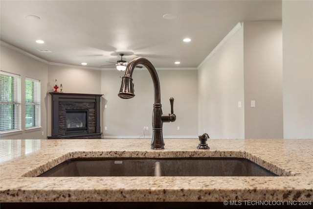 kitchen with a fireplace, light stone countertops, ornamental molding, and sink