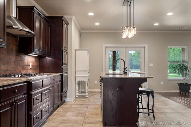 kitchen with a kitchen breakfast bar, appliances with stainless steel finishes, light stone counters, a kitchen island with sink, and sink