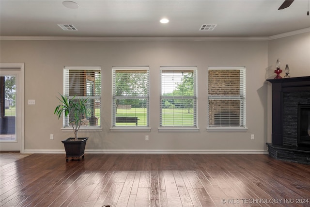 unfurnished living room featuring crown molding, a fireplace, a healthy amount of sunlight, and dark hardwood / wood-style floors