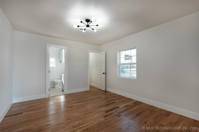 unfurnished bedroom featuring a notable chandelier, dark wood-type flooring, and connected bathroom