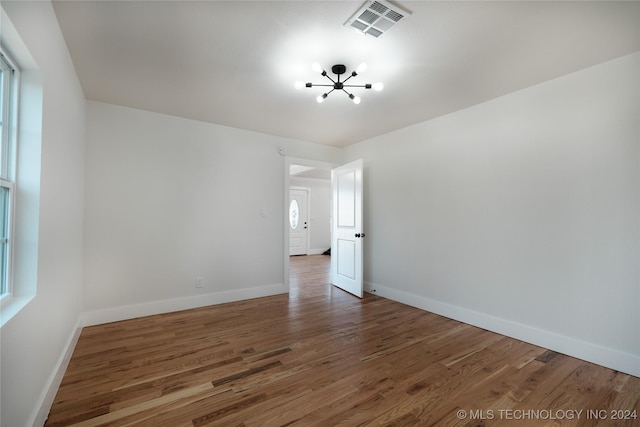 spare room with a wealth of natural light, dark wood-type flooring, and a notable chandelier