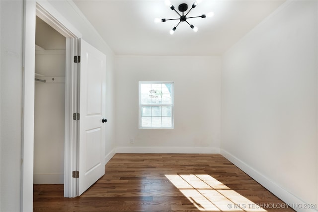 unfurnished bedroom featuring dark hardwood / wood-style flooring, crown molding, and a notable chandelier