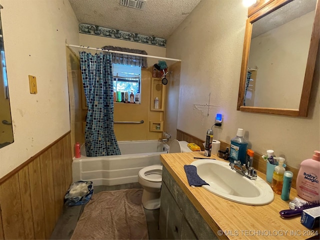 full bathroom with vanity, a textured ceiling, shower / bath combo with shower curtain, wooden walls, and toilet