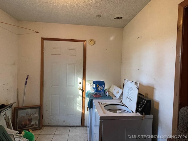 clothes washing area with light tile patterned flooring, separate washer and dryer, and a textured ceiling