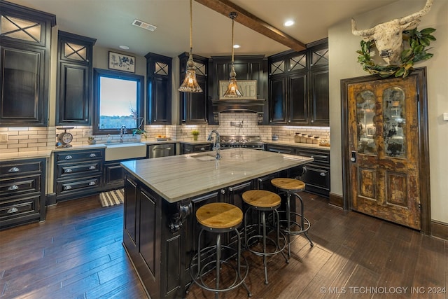 kitchen with tasteful backsplash, a kitchen island with sink, dark wood-type flooring, and decorative light fixtures