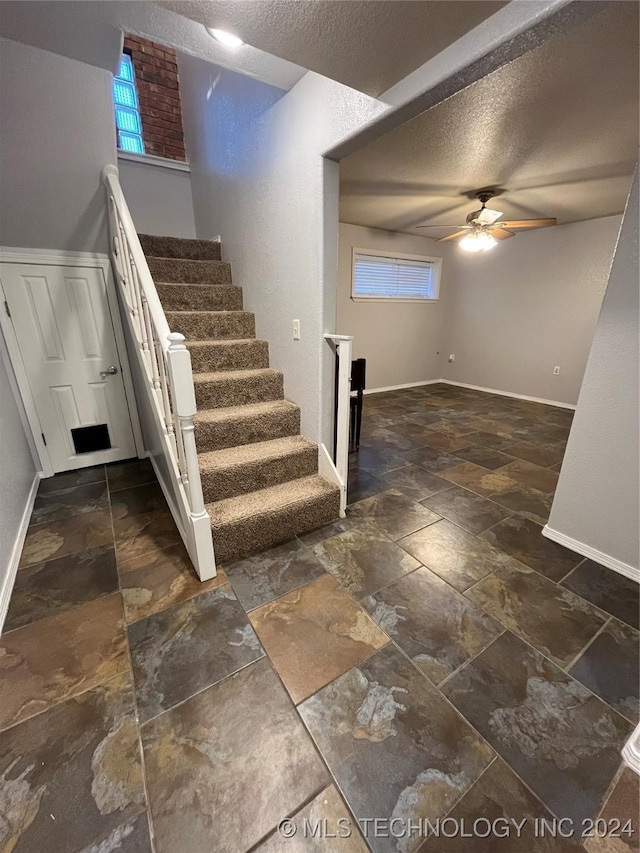 stairway featuring ceiling fan and a textured ceiling