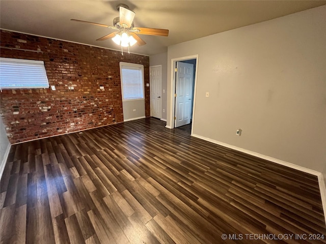 empty room with ceiling fan, dark wood-type flooring, and brick wall