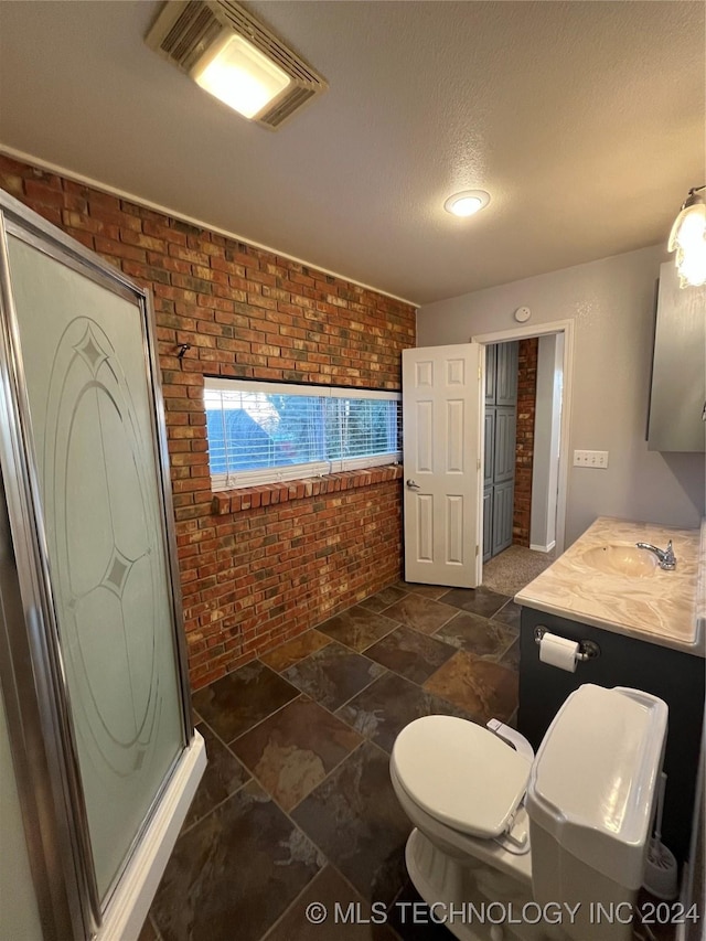 bathroom with a textured ceiling, vanity, toilet, and brick wall